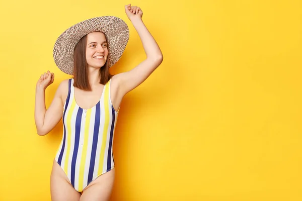 幸せなオーバー喜び女性身に着けていますストライプ水着と帽子孤立で黄色の背景ダンス喜び彼女の休暇コピースペースのためにプロモーションテキスト — ストック写真