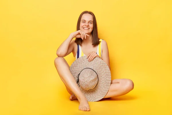 可愛いです笑顔喜び若いです女性身に着けていますストライプスイミングスーツ隔離された上に黄色の背景座っています彼女の帽子を見ますカメラ楽しみます彼女の夏休み — ストック写真