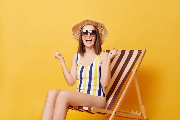 줄무늬 수영복을 노란색 배경에 고립된 의자에 휴양지로 여행하는 기뻐하며 주먹을 — 스톡 사진