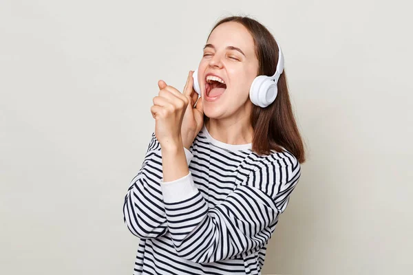 줄무늬 셔츠를 흥분된 헤드폰으로 음악을 마이크로 노래하는 척하는 — 스톡 사진