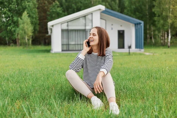 Outdoor Shot Attractive Positive Woman Talking Cell Phone Sitting Grass — Stock Photo, Image