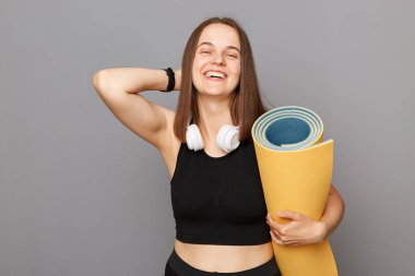 Elinde siyah tişört tutan mutlu bir kız gri arka planda izole bir şekilde poz veriyor yoga egzersizinden mutlu bir şekilde gülüyor..