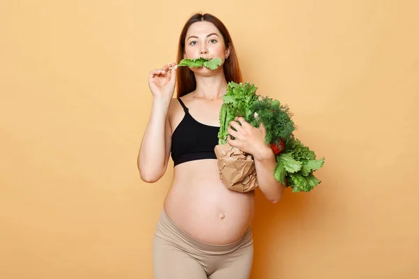 Hladová Těhotná Žena Přijímá Čerstvou Zeleninu Představuje Izolované Přes Béžové — Stock fotografie