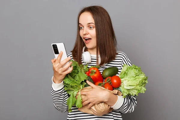 Удивительная Женщина Держит Овощи Изолированы Сером Фоне Держа Мобильный Телефон — стоковое фото