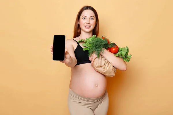 Winsome Kobieta Ciąży Gospodarstwa Świeże Warzywa Pozowanie Beżowym Tle Pokazuje — Zdjęcie stockowe