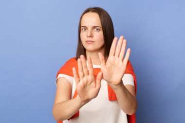 Beyaz tişört giyen, kazak giyen, mavi arka planda tek başına duran, avuçlarını uzatan ciddi ve katı bir kadın..