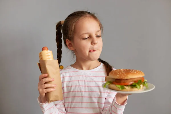 Голодная Забавная Маленькая Девочка Косичками Хот Догами Гамбургером Сером Фоне — стоковое фото