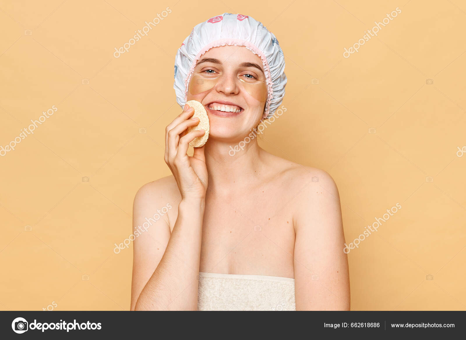Mujer atractiva joven con toalla de baño y gorro de ducha cara feliz  sonriendo mirando a la cámara lavando su cuerpo hablando ducha de pie  aislado sobre fondo beige