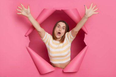 Aşırı neşeli, esmer, çizgili bluz giyen, yırtık pırtık pembe kağıt delikten bakan kadın kollarını kaldırdı ve 