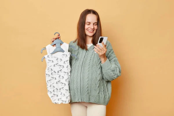 Dark Haired Pregnant Woman Wearing Knitted Sweater Holding Baby Bodysuits — Stock Photo, Image