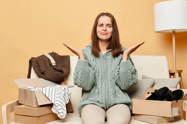 Sad Upset Woman Sitting Sofa Boxes Clothing Beige Wall Shrugging — Stock Photo, Image