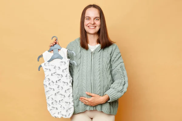 お願い正幸せな若いです妊娠中の女性とともにベージュバック上に隔離されましたバックグランドTouch彼女の腹見ますカメラ購入服のために彼女の将来の子供 — ストック写真