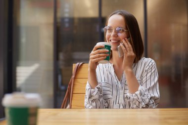 Boş vakitlerinde kafede otururken cep telefonuyla arayan genç ve çekici bir kadın. Şirin bir gülümseme ile kafede dinlenirken cep telefonuyla sohbet eden çekici bir kadın..
