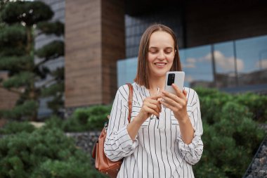 Güzel görünümlü, zarif kıyafetler giyen, elinde akıllı telefonuyla duran, olumlu duygularını ifade eden, haberleri okuyan, internette gezinen güzel bir kadın..
