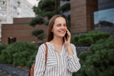 Çekici, güler yüzlü, neşeli bakışlı, mutlu yüzlü, cep telefonuyla konuşan, dışarıda konuşmanın tadını çıkaran, neşeli, pozitif bir kadın..