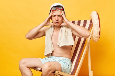 Hasta gömleksiz bir adam sarı arka planda izole edilmiş bir şekilde güvertede oturuyor. Güneşlenmek için saatlerce vakit harcıyor. Baş ağrısı azalıyor..