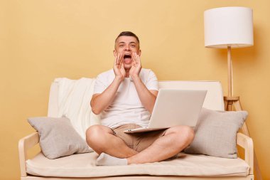Teknoloji iletişimi. Bilgisayar teknolojisi. Çevrim içi kullanıcı. Dizüstü bilgisayarda çalışan pozitif bir genç evde rahat bir koltukta oturup bağırarak anons yapıyor.