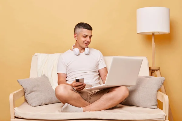 インターネットの閲覧 内務省だ レジャーサーフィン 自宅で快適なソファに座っているスマートフォンを使用して ラップトップコンピュータ上で働く積極的な魅力的な若い男 — ストック写真