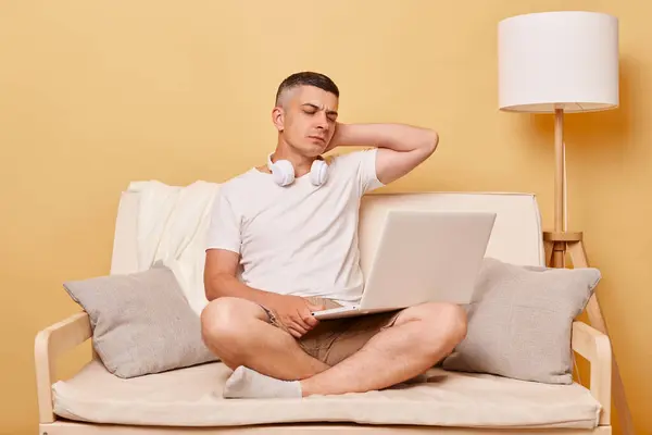 互联网连接 笔记本的工作 笔记本电脑的技术 疲惫不堪的年轻人坐在舒适的沙发上 在笔记本电脑上工作 感到疼痛 按摩疼痛的脖子 — 图库照片