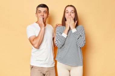 Şok olmuş genç karı koca, günlük kıyafetler giyip bej arka planda izole bir şekilde durmuş avuç içi korkuyla dolu ağızları kapatan korkunç bir şeye bakıyorlardı..