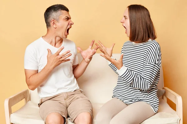 stock image Irritatedannoyed woman and man dressedcasuallysitting on sofa isolated over beige background arguing at home screaming with hate and anger, relationship problems.