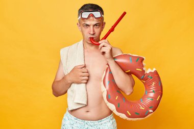 Dalgıç gözlükleri ve şnorkel takan kızgın bir dalgıç sarı arka planda izole edilmiş donut kauçuğu yüzüğüyle canı sıkkın bir ifadeyle kameraya bakıyor..
