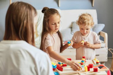 Ebeveyn-çocuk bağı. Mutlu aile zamanları. Oyuncak çocuk yuvası aktiviteleri. Ebeveynlik sevinç anları. Çocuklar anneleriyle birlikte evlerinde tahta ayıklayıcı oyuncaklarla oynuyorlar.