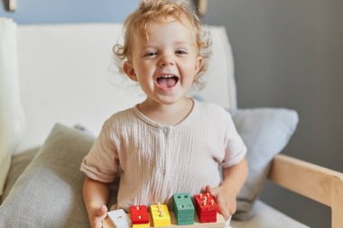 Bebeklerin yaratıcı oyunu. Montessori öğrenme araçları. Güler yüzlü sarışın kız bebek. Evinde tahta ayıklayıcı oyuncaklarla oynaşıyor.