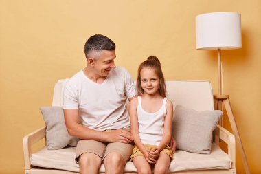 Pozitif yakışıklı adam, babası ve kızı gündelik giysiler giymiş bej arka planda oturan bir baba, kadın çocuğuna değer biçiyor..