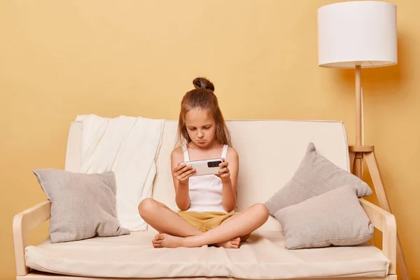 不幸な悲しい少女は ベージュウォールでオンラインビデオゲームをプレイするベージュウォールに対して自宅でソファーに座っているカジュアルな服を着て 口紅で座っている — ストック写真