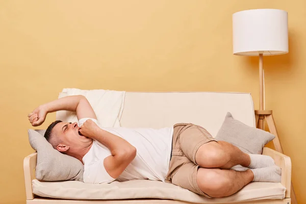 精疲力竭的男人躺在家里的沙发上打呵欠 用手掌捂住嘴 一夜未眠 疲惫不堪 — 图库照片