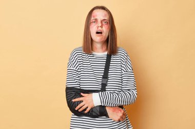 Sargılı şok olmuş genç bir kadın, sağlık sorunları yaşıyor. Kollarında güçlü ağrılar var. Araba kazaları, bej arka planda izole bir şekilde duran cildinde çürükler oluşturdu.