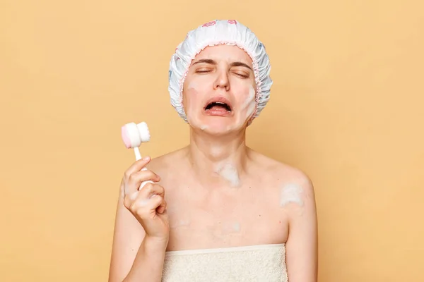 Płacząca Nieszczęśliwa Kobieta Czepku Stojąca Beżowym Tle Wykonująca Zabiegi Kosmetologiczne — Zdjęcie stockowe