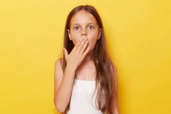 stock image Surprised amazed little girl with long hair standing isolated over yellow background looking at camera with big eyes covering mouth sees something shocked.