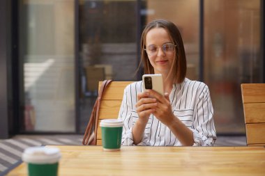 Resmî giyinmiş, gülümseyen sevimli iş kadını kahve içerken kahve içerken interneti kontrol ederken ara verdiğinde Socila ağlarını kontrol ediyor..