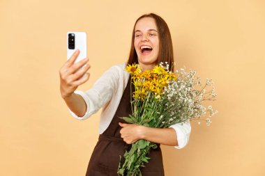 Çiçekçi dükkanında çiçekçiyle selfie çeken güzel bir kadın. Önlük takıp akıllı telefon kullanıyor..