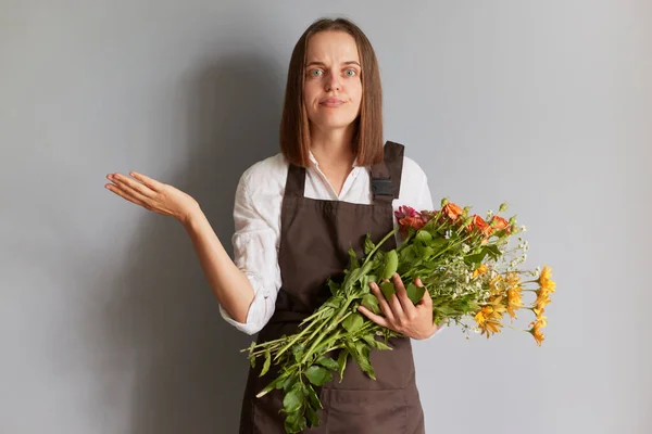 Intrigado Florista Feminino Confuso Vestindo Avental Marrom Segurando Flores Isoladas — Fotografia de Stock
