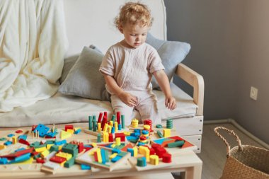 Küçük çocuğun büyük merakı. Neşeli bir anaokulu çocuğu yapmak. Bebek yuvası maceraları işte. Şirin dalgalı saçlı sarışın bebek evde ahşap eğitici oyuncaklar oynuyor..