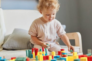 Renkli oyunlardan öğreniyorum. Küçük bir çocuk yuvası keşfi. Oyun alanı eğlencesi ve oyunları. Çekici dalgalı saçlı küçük sarışın bebek ev içinde ahşap eğitici oyuncaklar oynuyor..