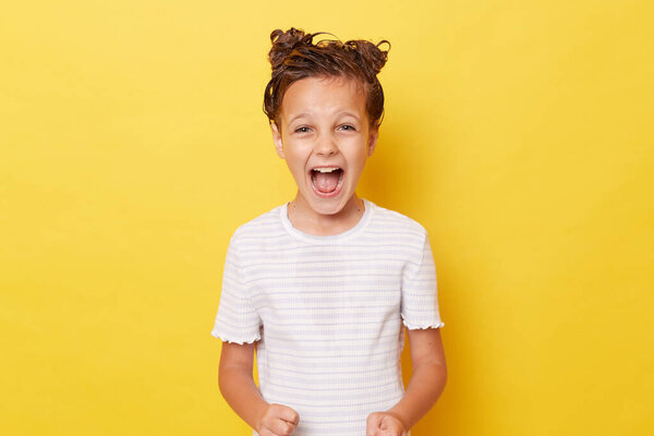 Безумно взволнованная девочка с шампунем на мокрых волосах в белой футболке, стоящей изолированно на желтом фоне и кричащая с позитивным выражением лица.