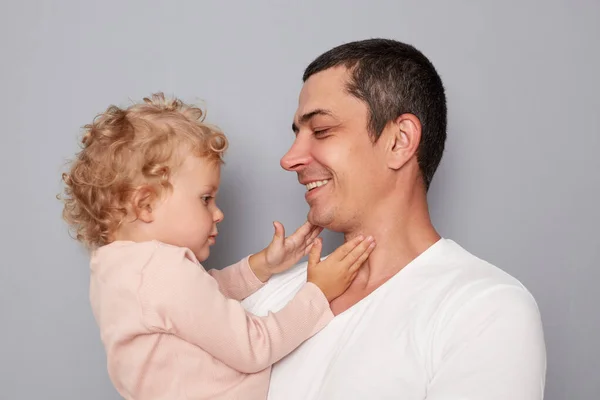Happy joyful people young man holding little toddler girl isolated on gray background looking at each other with love nad gentle expressing happiness positive emotions.