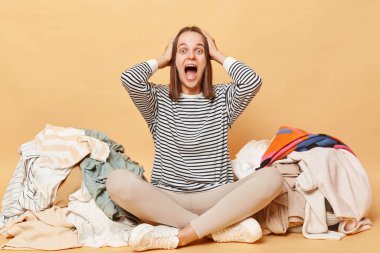 Kafkasyalı çılgın kadın, bej arka planda izole edilmiş, rengarenk kıyafetlerin yanında poz veriyor..