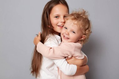 Happy funny girl sisters hugging and laughing standing isolated over gray background looking at camera with happy faces having fun playing together. clipart