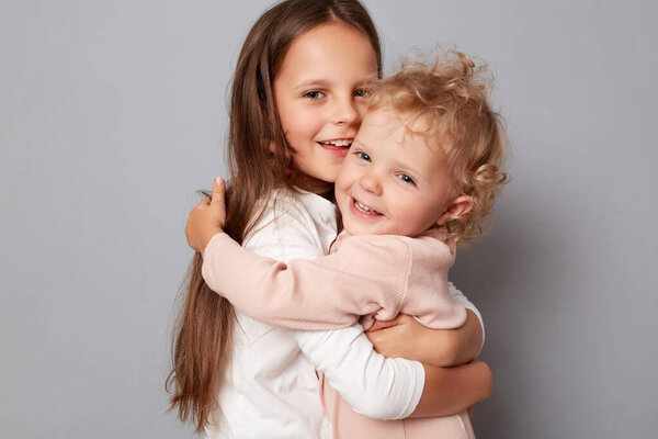 Happy funny girl sisters hugging and laughing standing isolated over gray background looking at camera with happy faces having fun playing together.