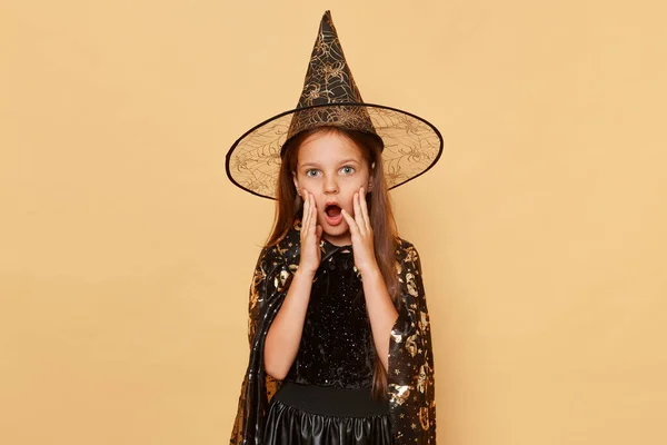 Шокированная Испуганная Маленькая Девочка Костюме Ведьмы Шляпе Карнавала Бежевом Фоне — стоковое фото