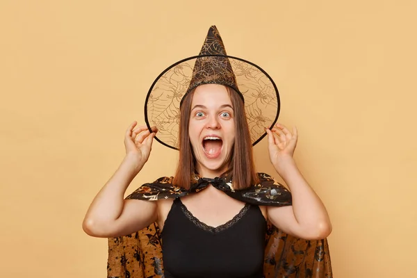 ハロウィーンを祝う魔女のコスチュームとカーニバル円錐形の帽子を身に着け ハロウィーンはハロウィーンの祭典で幸せを感じるベージュの背景の上に孤立しました — ストック写真