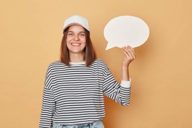 Soru sormakta tereddüt et. Fikrini paylaşmaktan çekinme. Yaratıcı kartpostal tasarımı fikri. Elinde boş beyaz konuşma balonu tutan gülümseyen kadın bej arka planda tek başına duruyor.