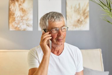 Sakin son sınıf öğrencisi, beyaz tişört ve gözlük takıyor. Sartphone ile geziyor. Kanepede oturuyor, dinleniyor, akıllı telefondan konuşuyor..