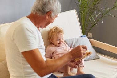 Oturma odası maceraları. Aile bağı. Mutlu bir yaşam tarzı. Eğitici oyun zamanı. Neşeli, gri saçlı adam evdeki kanepede torunuyla ahşap oyuncak oynuyor.