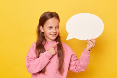 Sözlerini bekliyorum. Boş sohbet balonu. Düşünceler henüz dile getirilmedi. Sarı arka planda izole edilmiş pembe kazak giyen neşeli küçük kız boş konuşma baloncuğunu işaret ediyor.